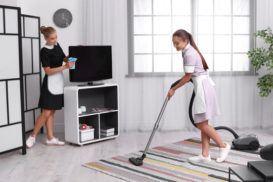 Professional chambermaids in uniform cleaning living room