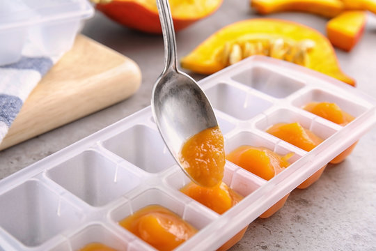 Putting healthy baby food into ice cube tray, closeup