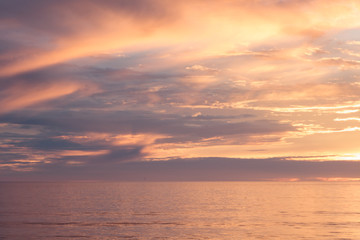 Sunset seascape, orange, blue, yellow, magenta, gold sky reflected in the sea pacific ocean, background photo of sun setting over horizon amid beautiful clouds