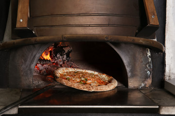 Oven with burning firewood and tasty pizza in restaurant kitchen