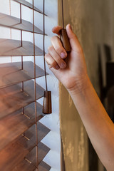 The woman's right hand holds one of the control strings of the wooden shutters on the window.