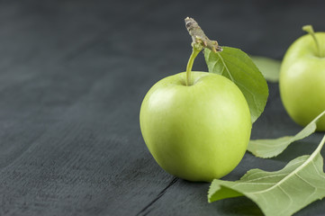 green fresh apple on black wooden backdrop and leaf