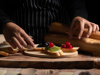 a female cooking preparing meal by using french bread with variety of fruit jam