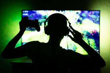 girl gamer in headphones in the dark on tv background. Ability to use as background. Silhouette © Anton