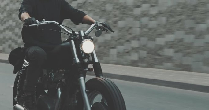 Motorcyclist drives on a motorcycle on the road in the city. Biker rides a vintage custom motorbike from 1970s . Urban lifestyle scene. Front view 4K video shooting by handheld gimbal
