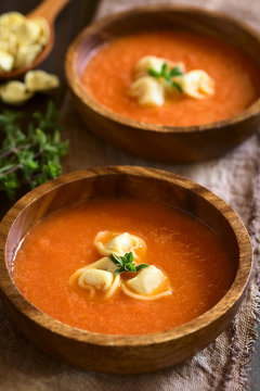 Homemade fresh cream of tomato soup with tortellini garnished with fresh oregano, served in wooden bowls, photographed with natural light (Selective Focus, Focus on the oregano on the first soup)