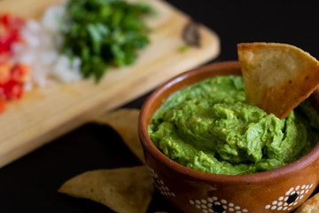 Guacamole mexicano tradicional de la salsa en el cuenco de arcilla y nachos en el fondo de un tablero de pizarra