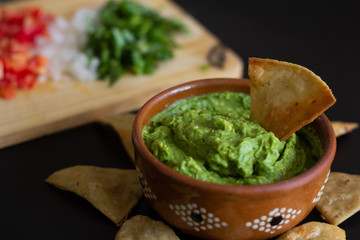 Guacamole mexicano tradicional de la salsa en el cuenco de arcilla y nachos en el fondo de un tablero de pizarra