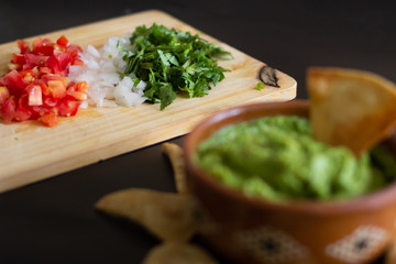Guacamole mexicano tradicional de la salsa en el cuenco de arcilla y nachos en el fondo de un tablero de pizarra