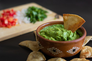 Guacamole mexicano tradicional de la salsa en el cuenco de arcilla y nachos en el fondo de un tablero de pizarra