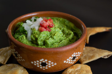 Guacamole mexicano tradicional de la salsa en el cuenco de arcilla y nachos en el fondo de un tablero de pizarra
