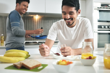 Homosexual Couple Eating Breakfast Cooking In Kitchen
