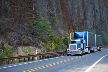 Big rig blue classic American bonnet semi truck with two covered black dry van semi trailers...