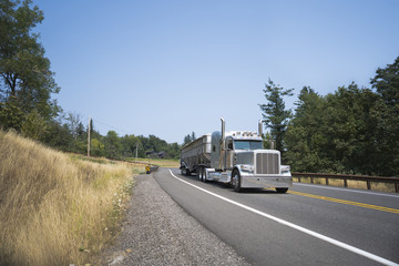 Big rig classic bonnet semi truck with long bulk semi trailer driving on the local road