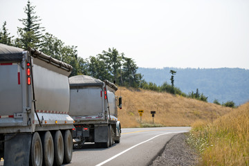Big rig semi truck tipper with two trailers driving with bulk cargo on the winding road