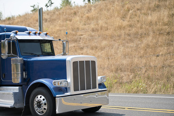 Cab of big rig blue bonnet semi truck driving on the road with hill