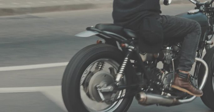 Motorcyclist drives on a motorcycle on the road in the city. Biker rides a vintage custom motorbike from 1970s . Urban lifestyle scene. Back view 4K video shooting by handheld gimbal