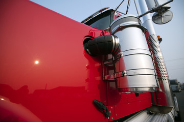 Part of red big rig semi truck tractor cab with chrome accessoriae
