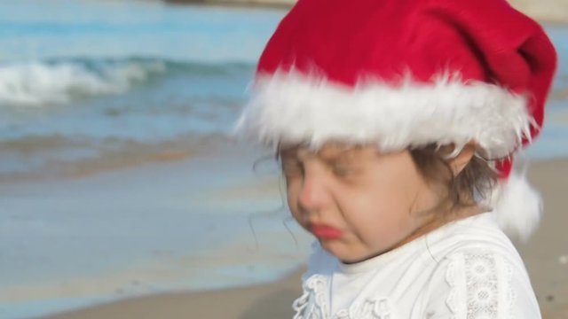 Charming child in Santa Claus hat on the beach.