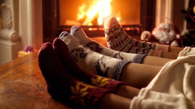 Closeup 4k video of family wearing woolen socks lying under blanket and warming by the fireplace