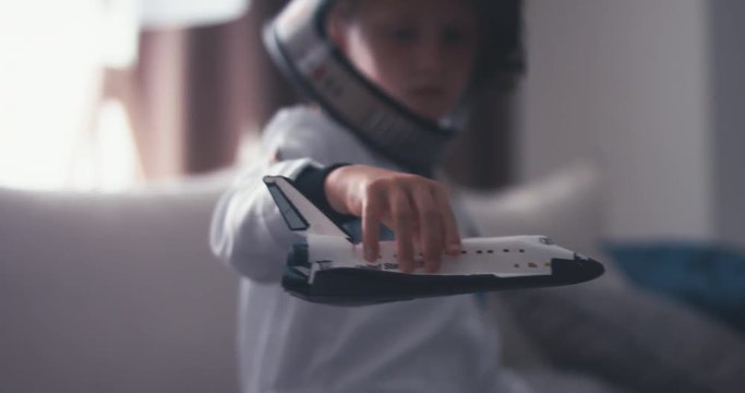 CU Cute little girl wearing astronaut suit playing with a toy space shuttle at home. Imagination concept. 4K UHD 60 FPS SLOW MO 