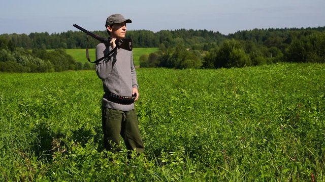 A hunter with a hunting gun stands in the field and looks around. 