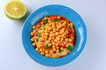 Close up dish Chickpea hummus and tahini dipped with olive oil, pepper, parsley, spices on a white table background. Hummus Traditional Middle Eastern food commonly served in a pita. Copy space.