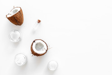 Coconut oil cosmetics for skin and hair care. Oil in small bottle, cream jar, halfs of coconut with shelf on white background top view copy space