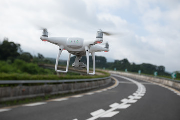 Naklejka na ściany i meble White drone with camera flying over highway