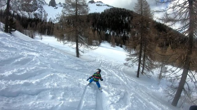 Freeride skiing. Little boy skiing in the wild. A 5 year old child enjoys a winter holiday in the Alpine resort. Stabilized shot. Slow motion.