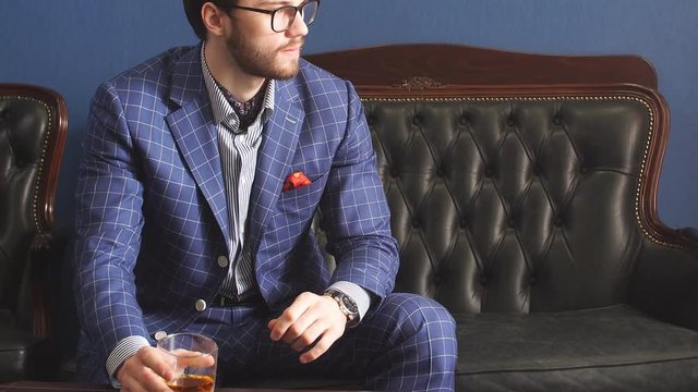 Handsome young man in a classic suit drinking whiskey.