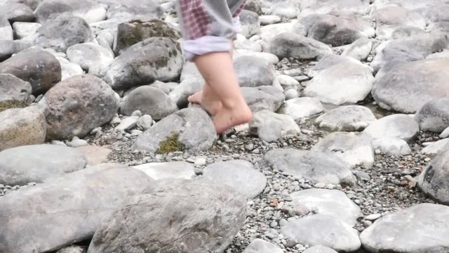 Feet of little girl run barefoot on a stone beach by the lake. slow motion