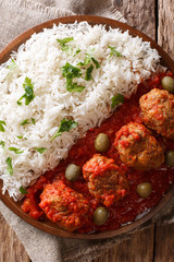 Traditional Soutzoukakia recipe (Greek baked Meatballs in tomato sauce) with a side dish of rice close-up. Vertical top view