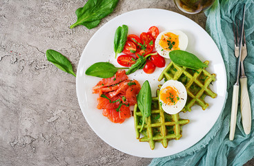 Savory waffles with spinach and egg, tomato, salmon in white plate. Tasty food. Top view. Flat lay