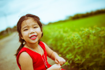 smiling kid girl in red dressing with green grass background process in vintage tone