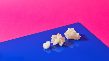 Crystals of natural mineral salt on a duotone pink-blue paper with shadows.