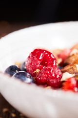 Close up of fresh red raspberry with ingredients for healthy organic dieting breakfast in a white bowl on a wooden table.
