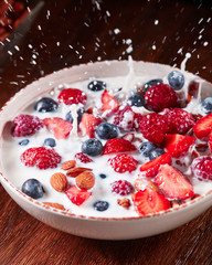 Splash milk from a bowl with a natural diet breakfast with granola, nuts and berries falling on a wooden table.