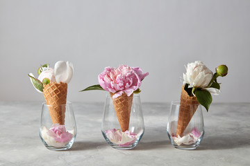 Wafer cones for ice cream with flowers peony and petals in a glasses on a gray table.