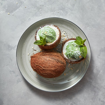 Freshly sweet green dessert in a coconut with green mint leaf and coconut chips on a plate on a concrete background.
