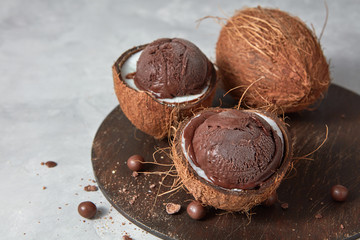 Delicious homemade chocolate ice cream in a coconut shell on a board on a gray concrete table....