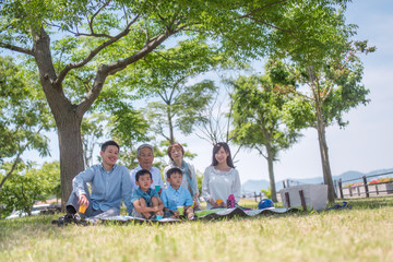 公園でレジャーシートに座りピクニックをする三世代家族