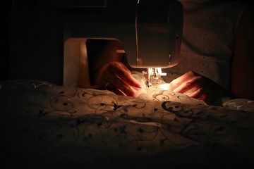 A woman sews at night on a sewing machine while everyone is sleeping