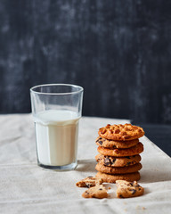 Homemade peanut cookies with chocolate chunks for Santa Claus, glass of milk on a textile towel on a black background.