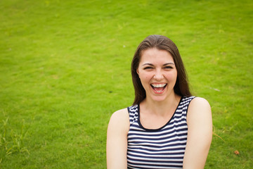 Naklejka na ściany i meble Beautiful happy brunette young woman smiling on green grass outside