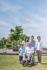 公園で微笑む車椅子のシニア男性と三世代家族