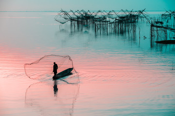 Silhouette of fishermen using coop-like trap catching fish in lake with beautiful scenery of nature morning sunrise. Beautiful scenery along seashore.