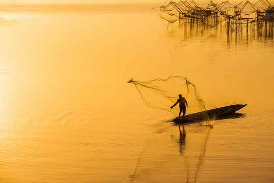 Silhouette of fishermen using coop-like trap catching fish in lake with beautiful scenery of nature morning sunrise. Beautiful scenery along seashore.