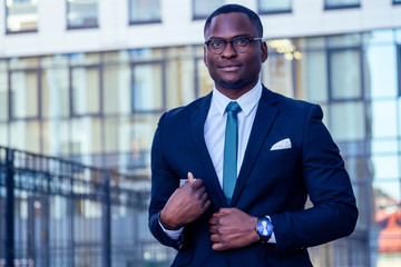 handsome and stylish afro american businessman in a fashionable jacket and a white shirt with a collar background of Manhattan glass offices cityscape