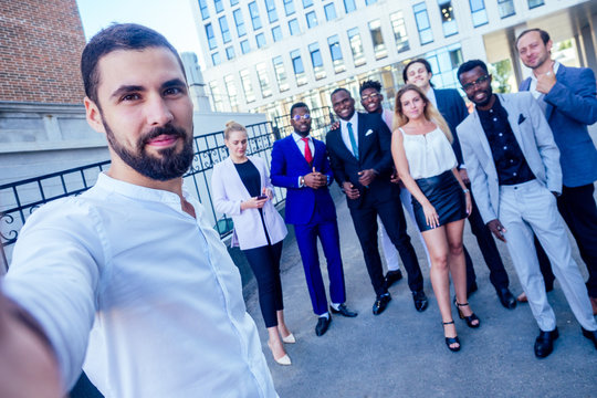 successful group of nine multinational businesspeople in a business suit looking into the phone and takes photos selfie standing company of people on the street .